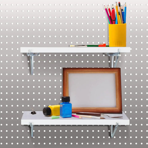 Four Pack White Fiberboard Pegboard Shelf Brackets with pens, a picture frame, and paint bottles on a pegboard.