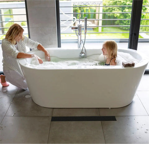 Bathroom scene with a mother and daughter in a tub, showing 24 Inch Linear Shower Drain With Accessories Rectangular Floor Drain Square Hole Pattern Cover Grate Removable SUS304 Stainless Steel CUPC Certified Matte Black High Flow No Fuss Easy Clean on the tiled floor.