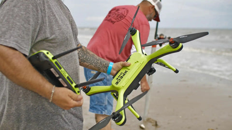 Angler holding a Waterproof Fishing Drone with 7 Pound Bait Release, HD Camera, ready to fly by the beach