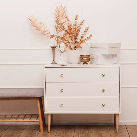 Stylish dresser with three drawers, white finish, decorated with golden accents and dried foliage for a chic look.