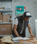 First aid kit, teal, 326-piece Be Smart Get Prepared; wall-mounted with man at desk wearing headphones.