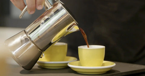 Hella Durable Stainless Steel Stovetop Espresso Maker pouring rich coffee into a yellow cup on a saucer.