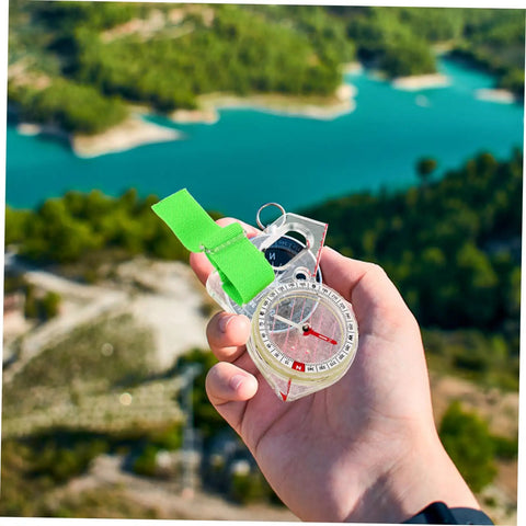 Thumb Type Directional Compass For Outdoor Navigation, Portable Hiking Tool held in hand overlooking a lake