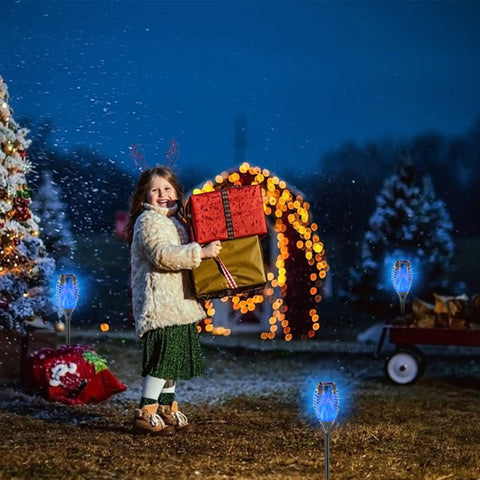 Child holding gifts in snowy garden adorned with Blue Solar Torch Lights Set, 8 Pack Outdoor LED Tiki Torches With Realistic Flickering Flame.