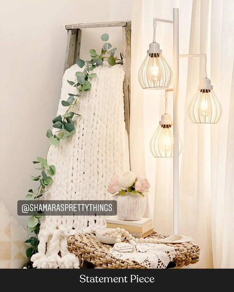 Teardrop Modern LED Floor Lamp with three cage shades next to a cozy decorated wicker table in a stylish interior setting.