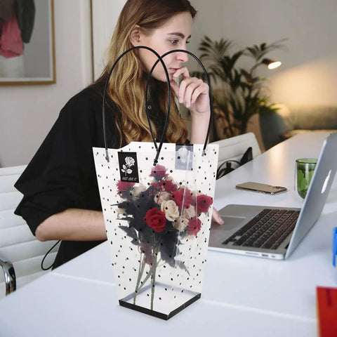 Plastic Bouquet Bags With Handles For Flower Packaging holding roses, displayed on a desk next to a woman using a laptop.