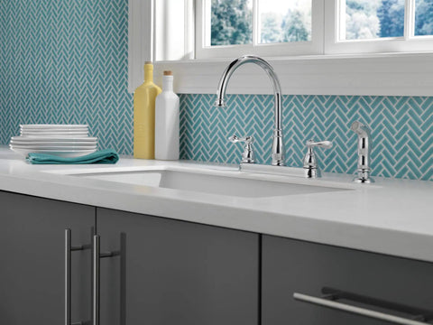 Windemere Chrome Kitchen Faucet With Side Sprayer For Four Hole 8 Inch Center Install Two Handle Classic Vibe Upgrade Durable Chrome Finish Drip Free Kitchen Sink installed on white counter with grey cabinets.