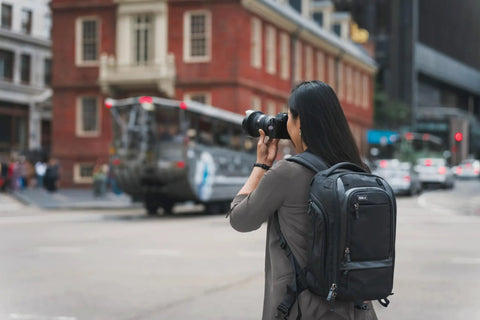 Person wearing 30L Camera Backpack For Photography And Video Gear With Full Front Panel Access, using camera in urban setting