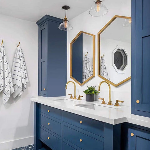 Modern bathroom with blue cabinets featuring gold brass drawer knobs, matching fixtures, and geometric mirrors.
