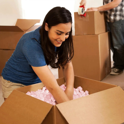 Person packing pink packing peanuts for shipping and moving, 14 cubic feet antistatic void fill cushioning supplies in box.