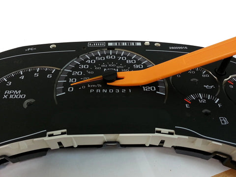 Automotive instrument cluster close-up with speedometer and tachometer; orange plastic pry tool resting on gauge