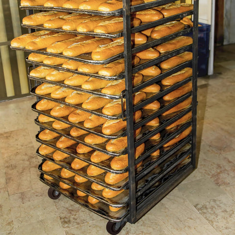 Bakery oven rack with high-temp swivel caster wheels full of freshly baked baguettes on mesh trays.