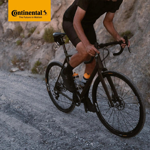 Cyclist riding a road bike on gravel, showcasing Continental tires; Premium Inner Tubes 700x32-47 (28x1.5-1.75) 42mm Presta Valve Pack Of 2 Fits 32-622 To 47-622 Durable Seamless Vulcanized, Quality Tested For Road Bike Wheels.