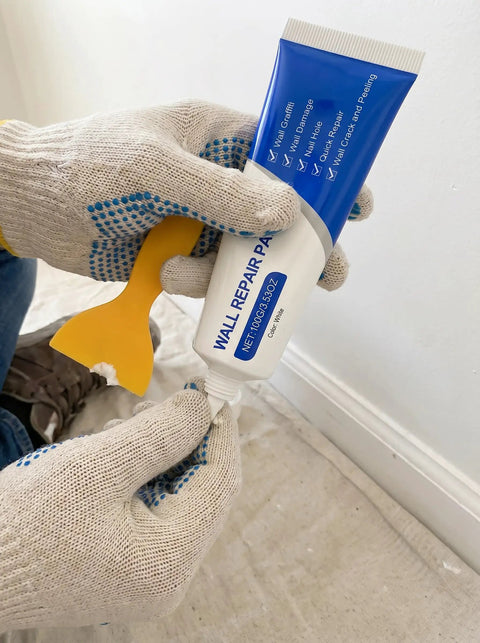 Hands holding Drywall Patch Repair Kit With Quick Drying Wall Mending Paste White Includes Scraper For Holes And Cracks Waterproof Heavy Duty Patch No Mess Diy Home Fix Pro Grade Set Of 2, showing mending paste tube and yellow scraper.