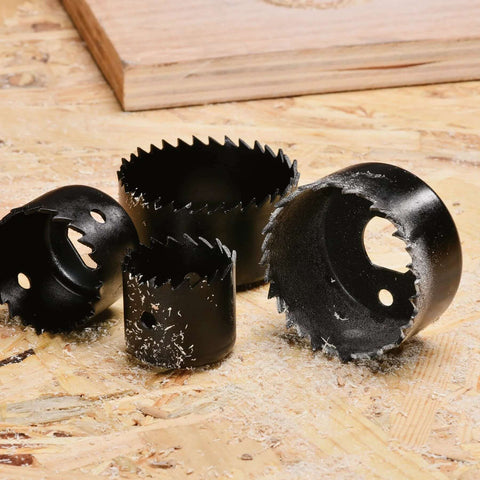 Front view of black metal hole saws in various diameters with jagged teeth on a wooden work surface.