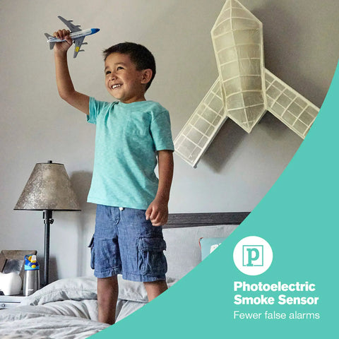 Child playing with toy airplane in bedroom with focus on photoelectric smoke sensor feature advertised in image.