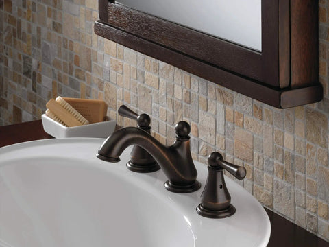 Oil-rubbed bathroom faucet with dual handles on white sink, set against a tiled wall.
