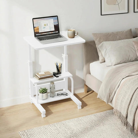 Space Saver C Shaped Laptop Desk On Wheels For Small Spaces White 24 Inch Height Adjustable With 2 Tier Storage Shelves Mobile Under Sofa Or Bed Setup next to a bed with laptop and coffee cup.