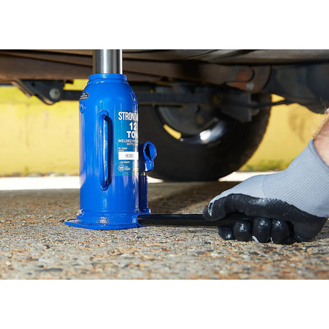 Badass 12 Ton Hydraulic Bottle Jack With High Grade Steel Welded Base in use, lifting under a vehicle on a gravel surface.