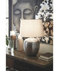 Magalie Contemporary Table Lamp In Antique Silver With Hammered Aluminum Construction on table with books and candles.
