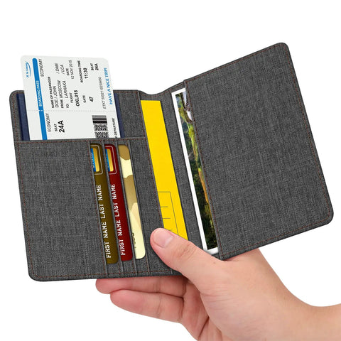 Hand holding slim RFID blocking passport holder with card slots in denim charcoal brown, open showing cards and boarding pass.