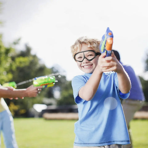 Boy wearing Dope 2 Pack Kiddo Protective Eyewear With Killer Wind Blocking Frame And Ultra Comfy Foam Cushions For Foam Blaster Nerf Games Clear Lens Safety Goggles With Adjustable Strap shooting water gun outdoors.