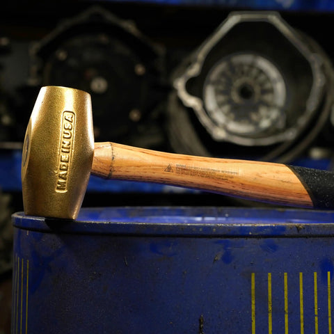 Non Sparking Brass Hammer 18 Inch 5 Pound USA Made With Wood Handle And Double Faced Head, resting on a blue barrel.
