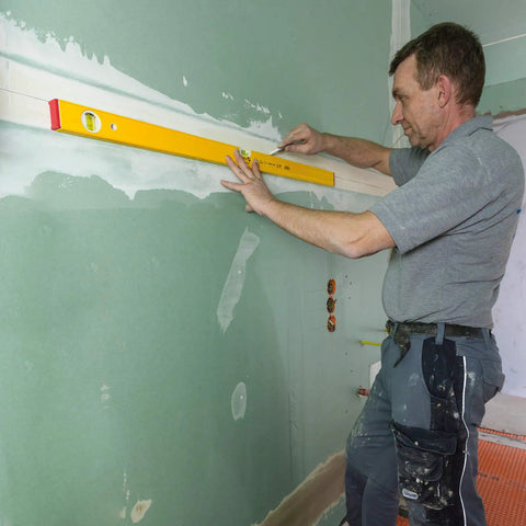 Professional 12 Inch Spirit Level Featuring Rock Solid Aluminum Build And Razor Sharp Vials used by a tradesman checking wall alignment.