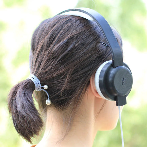 Woman wearing black and white headphones while her hair is tied back with a gray band and pearl accents.