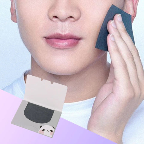 Man using dual pack oily skin blotting sheets, holding one against his face, panda design packaging visible.