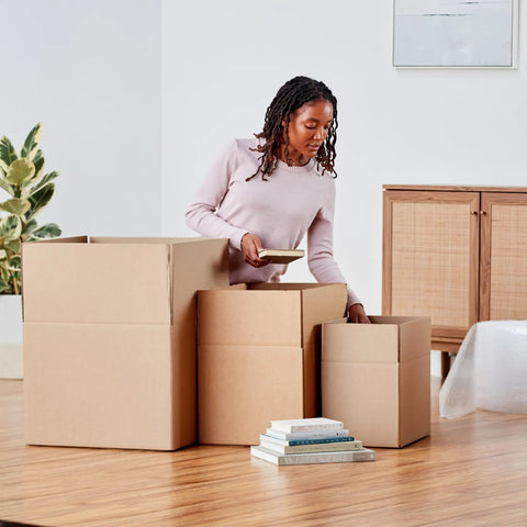 Woman organizing books into Rock Solid Large Cardboard Moving Boxes For Easy House Moves And Reliable Storage Heavy Duty Corrugated Packing Cartons.