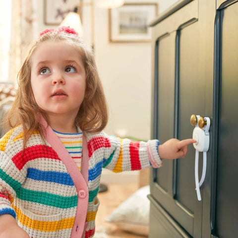 OutSmart Flex Lock Childproof Cabinet Locks White 2 Pack installed on dark cabinet, toddler touching decoy button