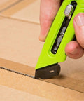 Close-up of Heavy Duty Box Cutter Utility Knife with Tape Splitter and Film Cutter cutting box, ergonomic handle, 3-position retractable blade.