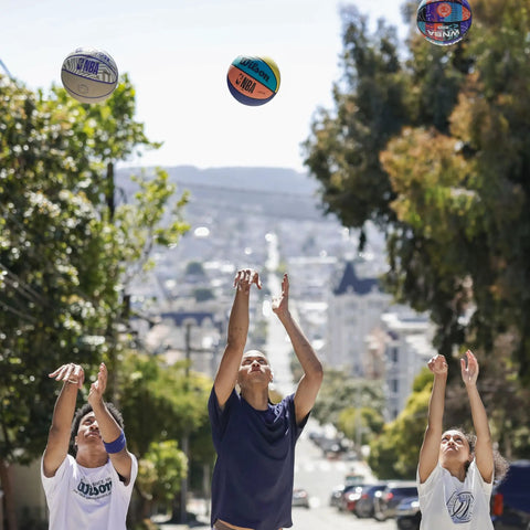 People shooting the Official DRV Series Basketball 27.5 Inch Size 5 in brown with rugged outdoor cover on a street.
