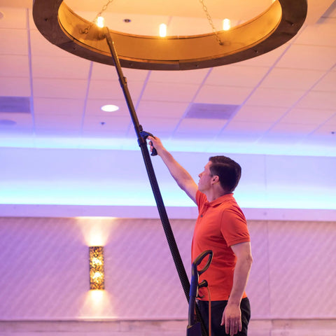 Man using Powr-Flite Borelli Dual Pro Upright Vacuum With HEPA Filtration to clean a high chandelier in a commercial space.