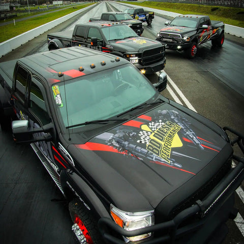 Four black diesel trucks on a racetrack showcasing performance and design.