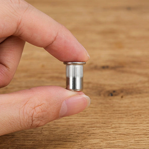Hand holding an M6 knurled stainless steel rivet nut, part of 50 Pack M6 Knurled Stainless Steel Rivet Nuts Blind Rivet Nuts for Metal and Wood Installation Built to Last Heavy Duty Vibration Proof Threaded Inserts for Automotive DIY Furniture Projects and Industrial Use