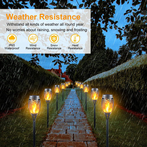 Mini Solar Torch Lights With Flickering Flame Upgraded 12 LED Outdoor Waterproof Tiki Torches illuminating a rainy pathway