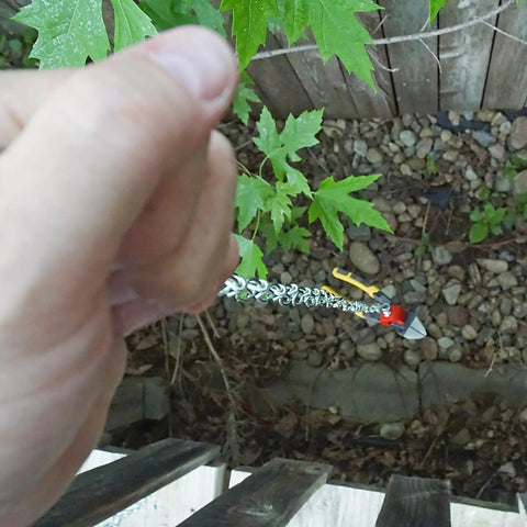 Hand holding a tool near a cable, with leaves and rocks visible below.