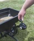 Tow Behind Broadcast Spreader With 85 Lb Capacity For Lawns, hand adjusting tractor seat on/off control near grass