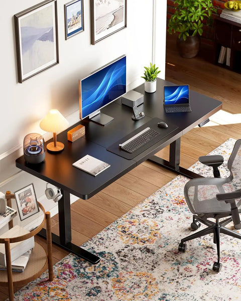 Home office setup with Electric Standing Desk 71 By 30 Inch Built To Be A Workhorse With Quiet Brushless Motor Height Adjustment Four Memory Presets Sit Stand Home Office Computer Desk With Thick T Shaped Frame, featuring dual monitors, keyboard, mouse, and decor, against an art-adorned wall.