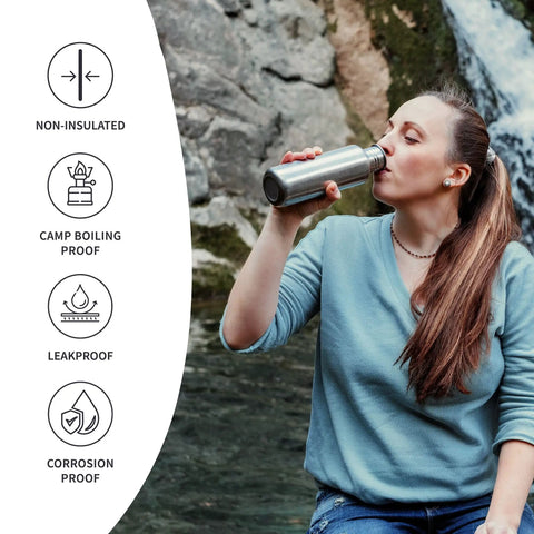Woman drinking from Straight Up Reliable Stainless Steel Water Bottle 32 Oz Single Wall Reusable Drinkware by a waterfall.