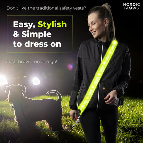 Rechargeable LED Reflective Safety Sash Featuring Three Custom Flashing Modes To Keep You Lit Safe And Street Sharp While Cruising The Sidewalks Or Cranking Out Night Miles, worn by a woman walking a dog.