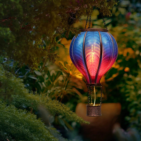 Blue Purple Hot Air Balloon Solar Lantern for Garden Decor lit with flickering flame hanging among greenery outdoors at night