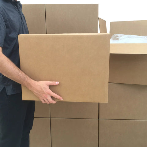 Person holding a large Rock Solid cardboard moving box, showcasing heavy-duty corrugated material, ideal for storage and relocation.