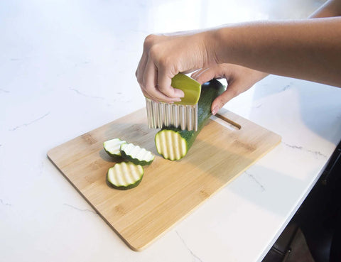 Joie crinkle cutter knife with green handle slicing zucchini on a wooden cutting board; stainless steel blade