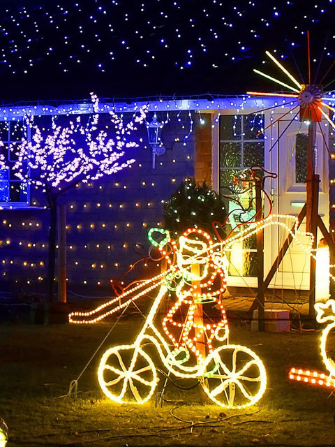 Christmas light display with Santa on a bicycle, glowing LED lights and a decorated tree, festive outdoor holiday scene.
