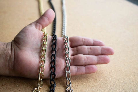 Hand holding 12 gauge solid steel twist link fixture chains in different finishes, part of the 164 ft reel for pendant lighting and decor.