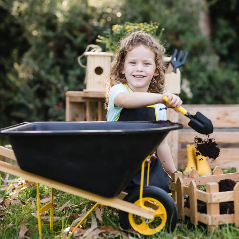 Child playing with six piece kid friendly wheelbarrow and garden tool set with apron and gloves for backyard play