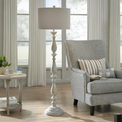 Bernadate Cottage Candlestick Floor Lamp, 61 Inch Tall, whitewashed cast resin base with drum shade next to a gray armchair